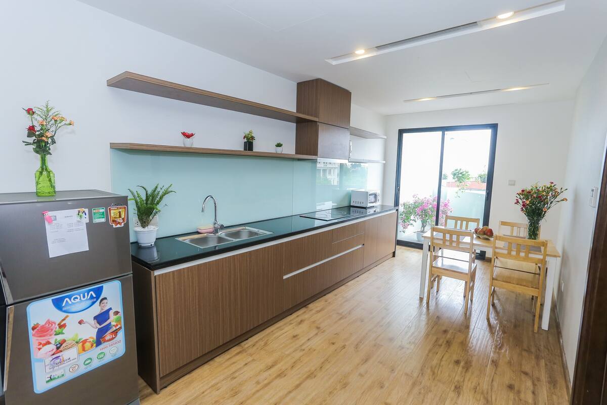 A modern kitchen with wooden cabinets, a stainless steel refrigerator, and a glass countertop.