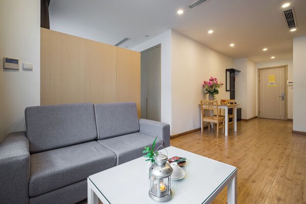 A modern living room with a grey sofa, a white coffee table with a lantern, and a wooden dining table with chairs.