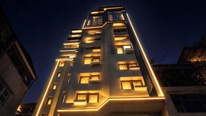A modern hotel with a prominent entrance, a staircase leading up to the lobby, and a flag displayed outside. - Ficus Suites Apartment (Hanoi)