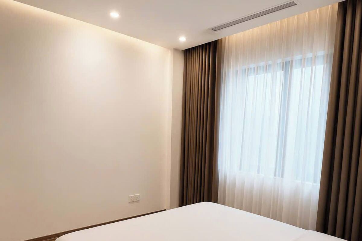 A hotel room with a large bed, a window with curtains, and a wooden floor.