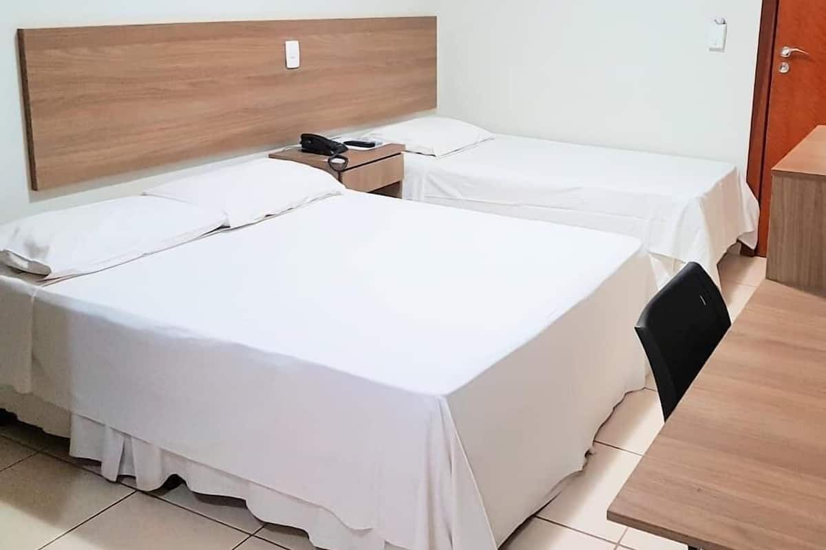 Ein Hotelzimmer mit zwei Einzelbetten, einem Holzkopfteil, einem Nachttisch mit Telefon und einem kleinen Schreibtisch mit Stuhl.