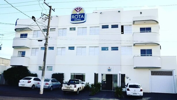 Un edifici de diverses plantes amb un rètol que diu "ROTA HOTELS". Diversos cotxes estacionats al davant i un cel clar a dalt.