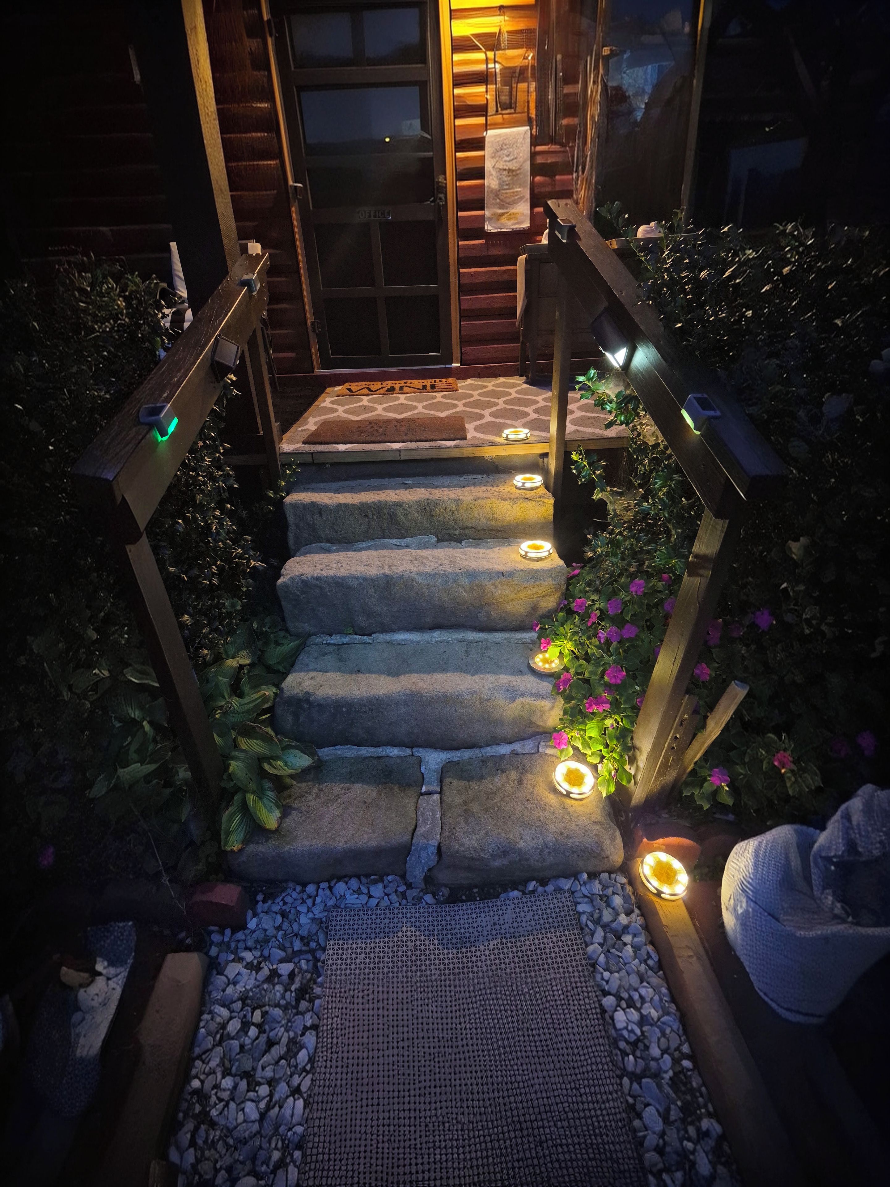 A set of stone steps leading to a wooden door, flanked by wooden railings with integrated lighting.