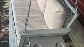 A white wicker swing bed with cushions, a small table, and a trash can nearby. - Log Cabin in the Field (Huntington)