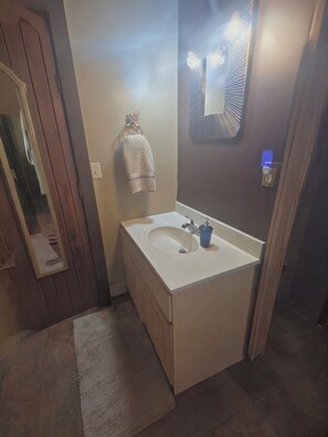 A bathroom with a white sink, a towel hanging on the wall, and a mirror with lights. - Log Cabin in the Field (Huntington)
