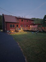 Un edificio de madera de dos pisos con un porche, una pequeña terraza y un camino de entrada pavimentado.