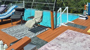 A poolside area with lounge chairs, a covered seating area, and a wooden deck. - Log Cabin in the Field (Huntington)