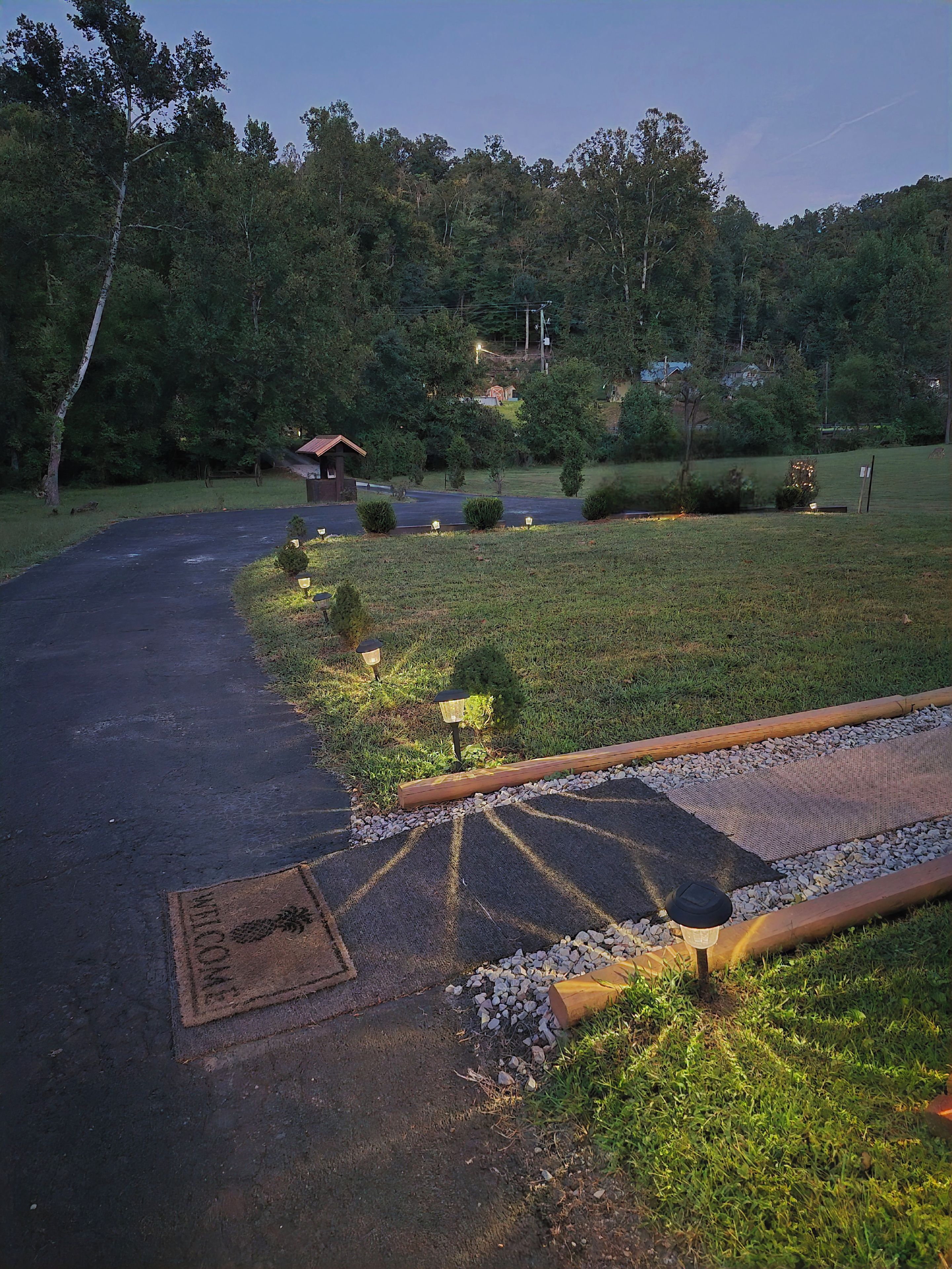 A paved driveway leading to a building with a red roof, surrounded by greenery and trees.