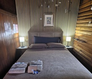 A neatly made bed with a headboard, two bedside lamps, and a framed picture above it. - Log Cabin in the Field (Huntington)