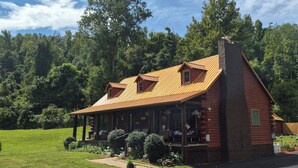 A rustic log cabin with a porch, surrounded by a well-maintained lawn and trees. - Log Cabin in the Field (Huntington)
