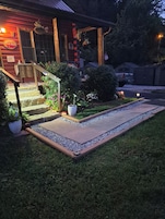 Una casa de madera con un porche, escalones y un pequeño jardín con plantas en macetas y flores.