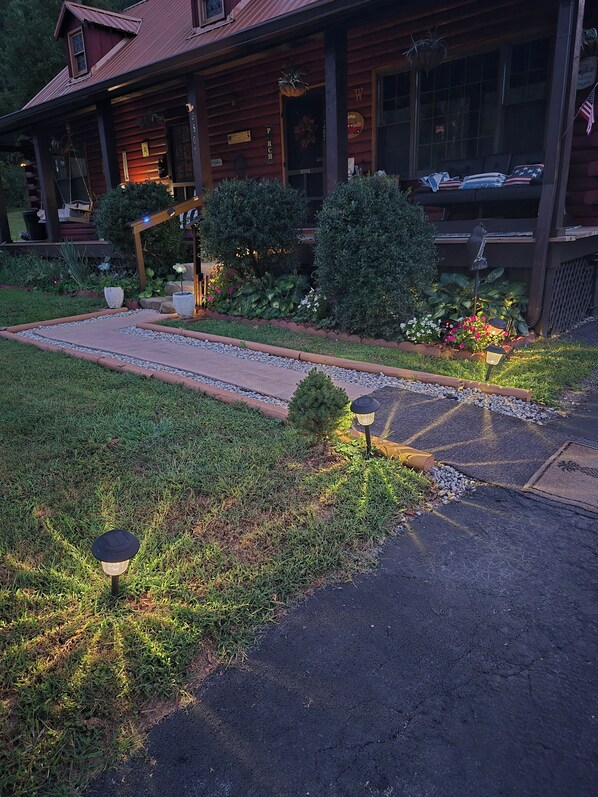 A wooden cabin with a porch, a garden with potted plants, and a pathway leading to the entrance. - Log Cabin in the Field (Huntington)