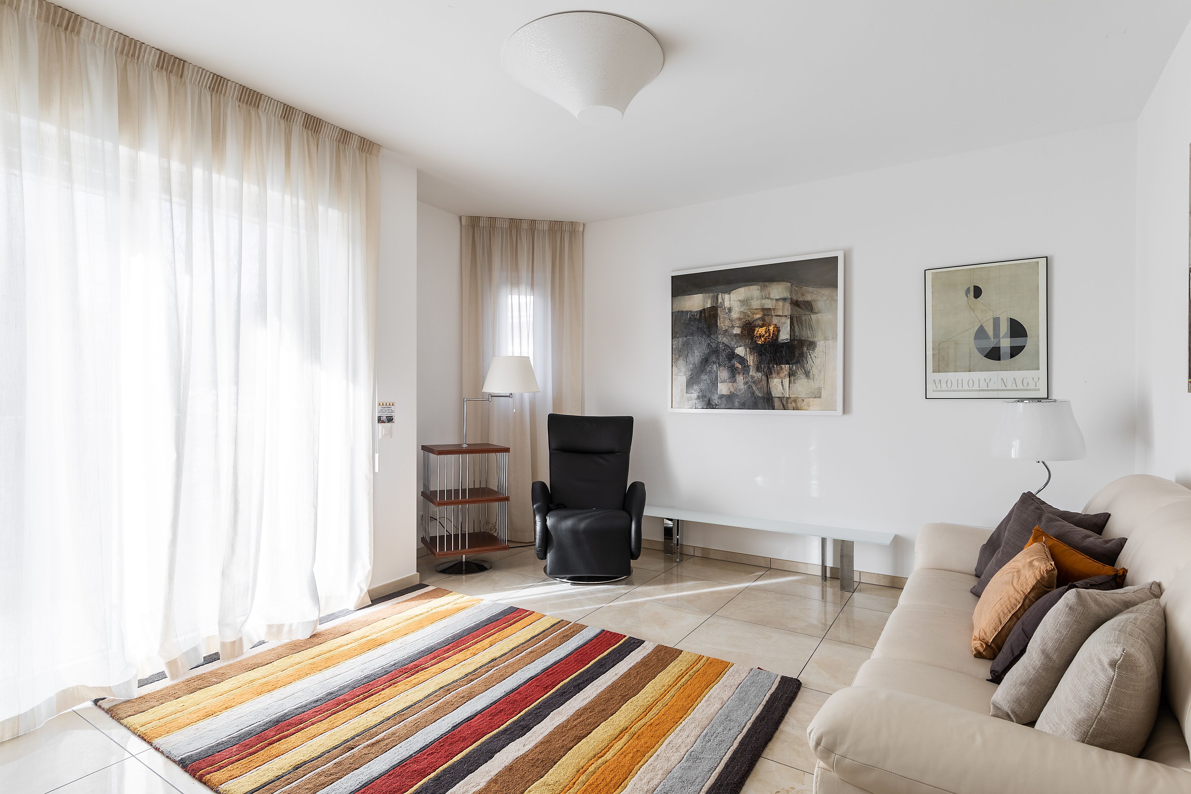 Un salon moderne avec un canapé, un fauteuil noir, un tapis rayé aux couleurs vives et des œuvres d’art accrochées aux murs.