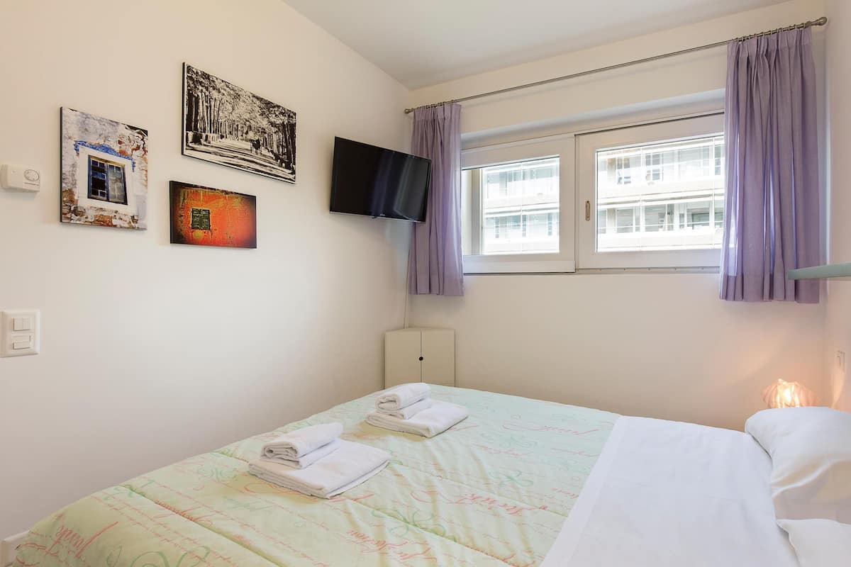 Habitación de hotel con cama, televisión de pantalla plana, ventana con cortinas moradas y obras de arte en la pared.
