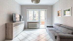 Una sala de estar moderna con un sofá gris, un mueble de madera, un televisor y una ventana con vistas a edificios.