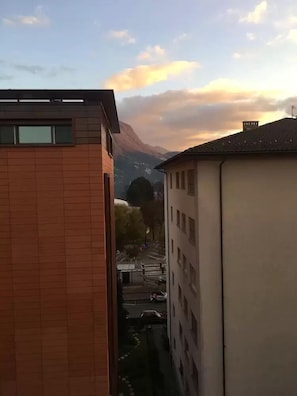 Una calle estrecha flanqueada por edificios, cielo despejado y montañas a lo lejos.