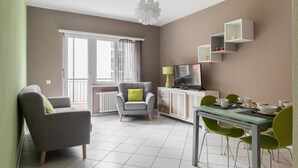 Una sala de estar moderna con un sofá gris, una mesa de comedor con sillas verdes, un televisor y una lámpara de techo original.