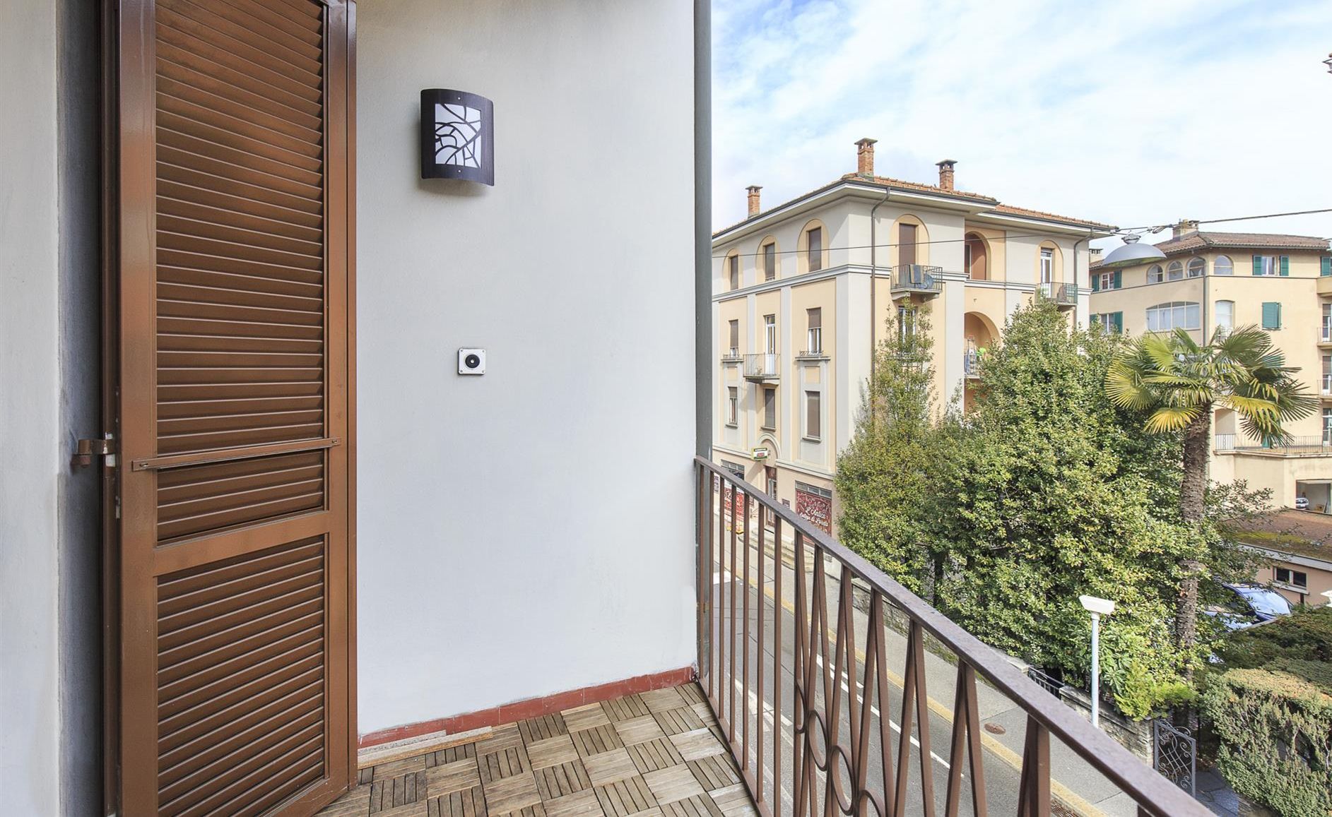A balcony with a wooden door, a wall-mounted light fixture, and a view of adjacent buildings.