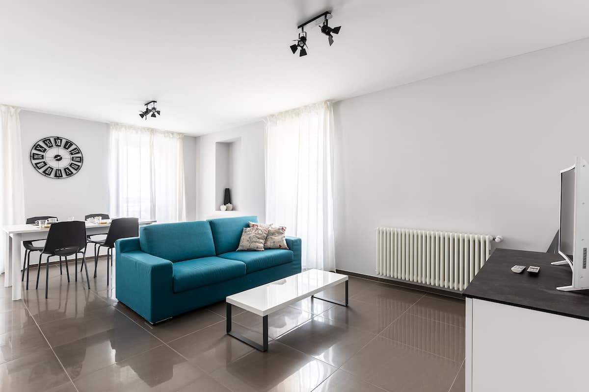 Una sala de estar moderna con un sofá azul, una mesa de centro blanca y un comedor con sillas y una mesa.