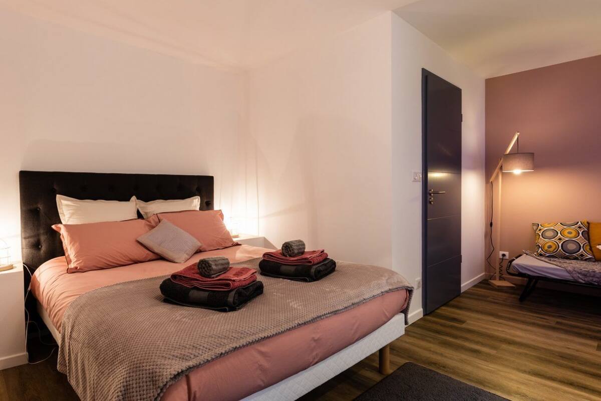 A modern bedroom with a large bed, bedside tables, a nightstand, a lamp, and a door.