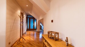 A hallway with wooden flooring, a coat rack, a wooden table with a lantern, and a door leading to another room.