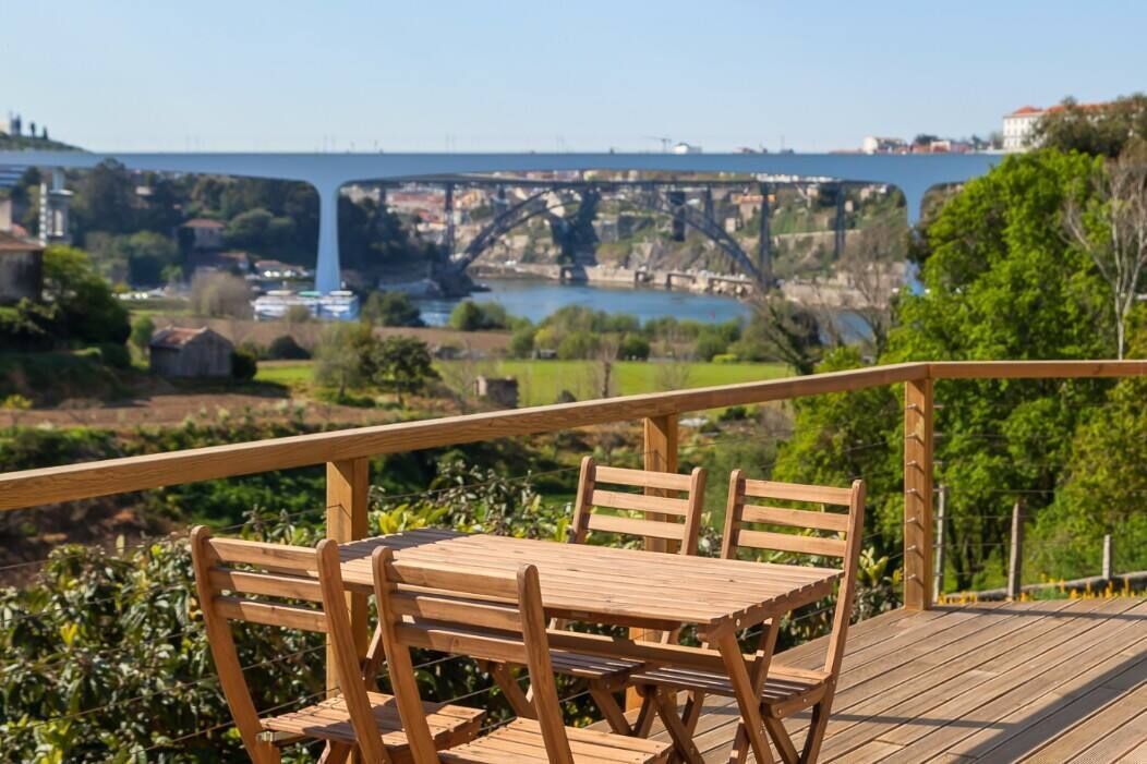 A wooden deck with a table and chairs overlooking a river and a bridge.