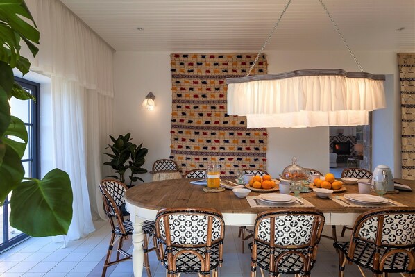 A dining area with a round wooden table, patterned chairs, a hanging light fixture, and a colorful tapestry on the wall. - Quinta de Sá (Vila Nova de Gaia)