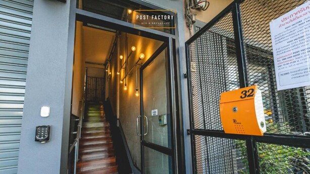 Entrada de un edificio tipo fábrica con una escalera que conduce al interior, un puesto de seguridad y una reja de metal.