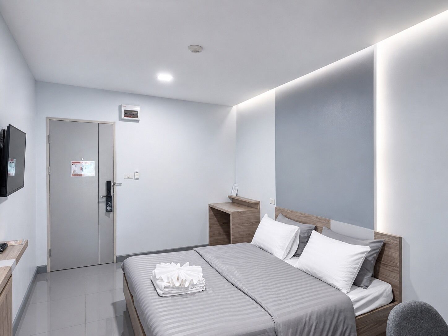 A modern hotel room with a bed, bedside table, and a flat-screen TV mounted on the wall.