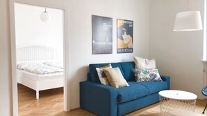 A modern living room with a blue sofa, a white bed, and two posters on the wall. - Lovely Apartment directly at Naschmarkt (Vienna)