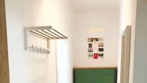 A hallway with a wooden herringbone floor, a green cabinet, a white chair, and a wall-mounted rack. - Lovely Apartment directly at Naschmarkt (Vienna)