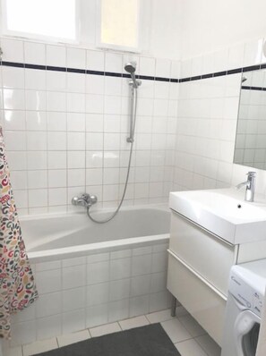 A modern bathroom with a white bathtub, a shower, and a sink.