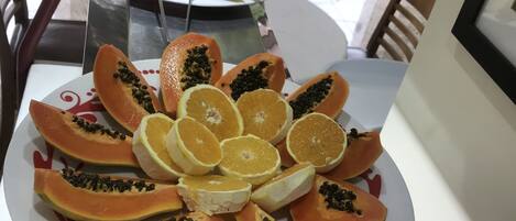 Une table sur laquelle est disposée une assiette de fruits comprenant de la papaye et des oranges. On aperçoit une porte vitrée et des sièges d’extérieur à l’arrière-plan.