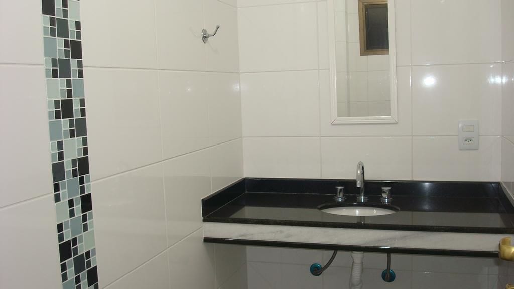 A bathroom with white tiled walls, a black countertop sink, and a small window above the mirror.