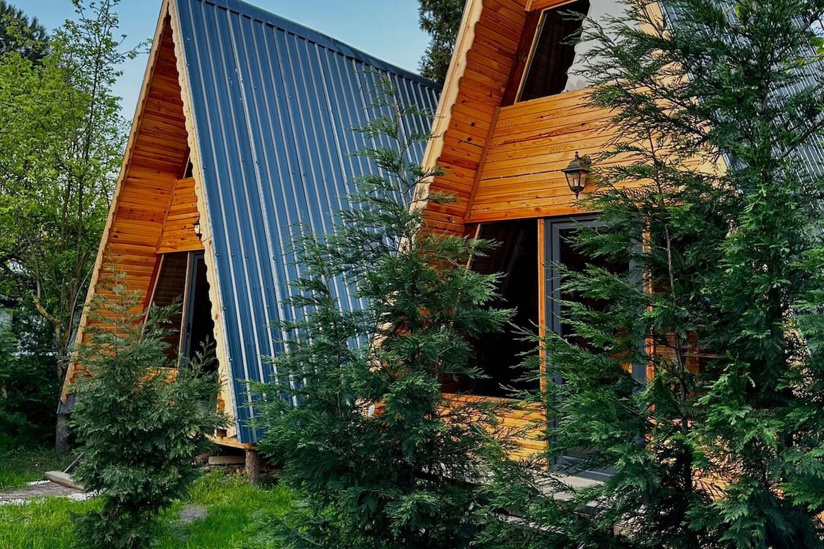 Ein modernes Gebäude mit einem dreieckigen Dach und einer Holzfassade, umgeben von üppigem Grün.