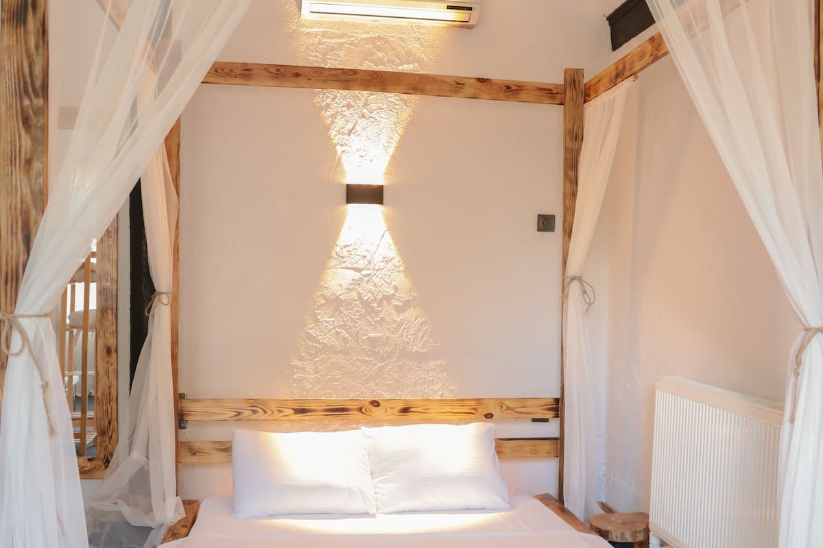 Ein Bett mit Holzrahmen, weißer Bettwäsche und transparenten Vorhängen.