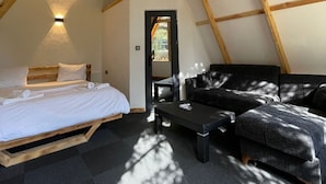 Une chambre à coucher confortable, aménagée en style « loft », avec un lit, un canapé en cuir noir, une petite table et un luminaire suspendu.