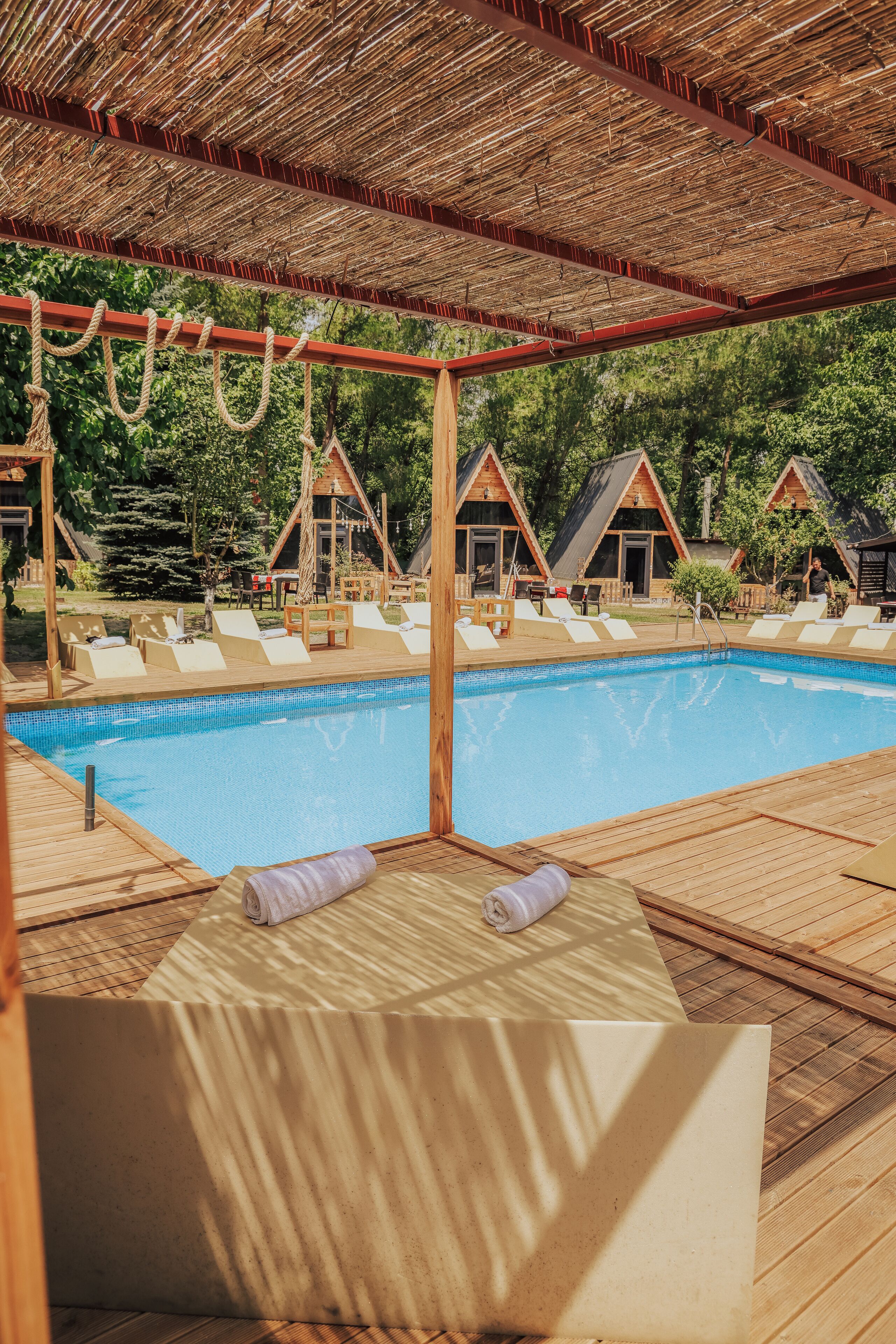 Ein Poolbereich mit Holzterrasse, Liegestühlen und einer Struktur mit Reetdach.