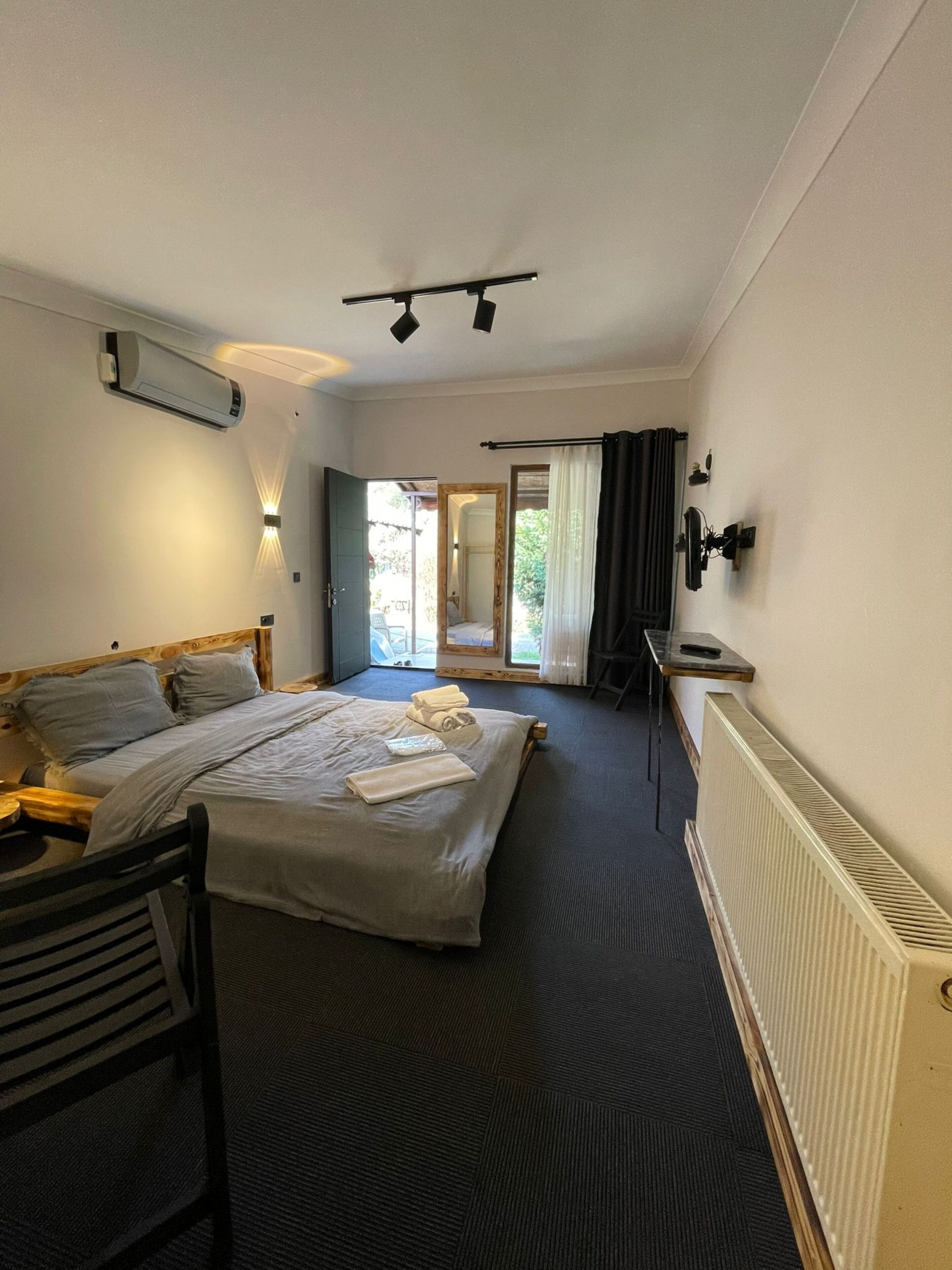 Ett hotellrum med en säng, ett skrivbord, en stol och ett element. Det finns ett fönster med gardiner och en dörr som leder ut.