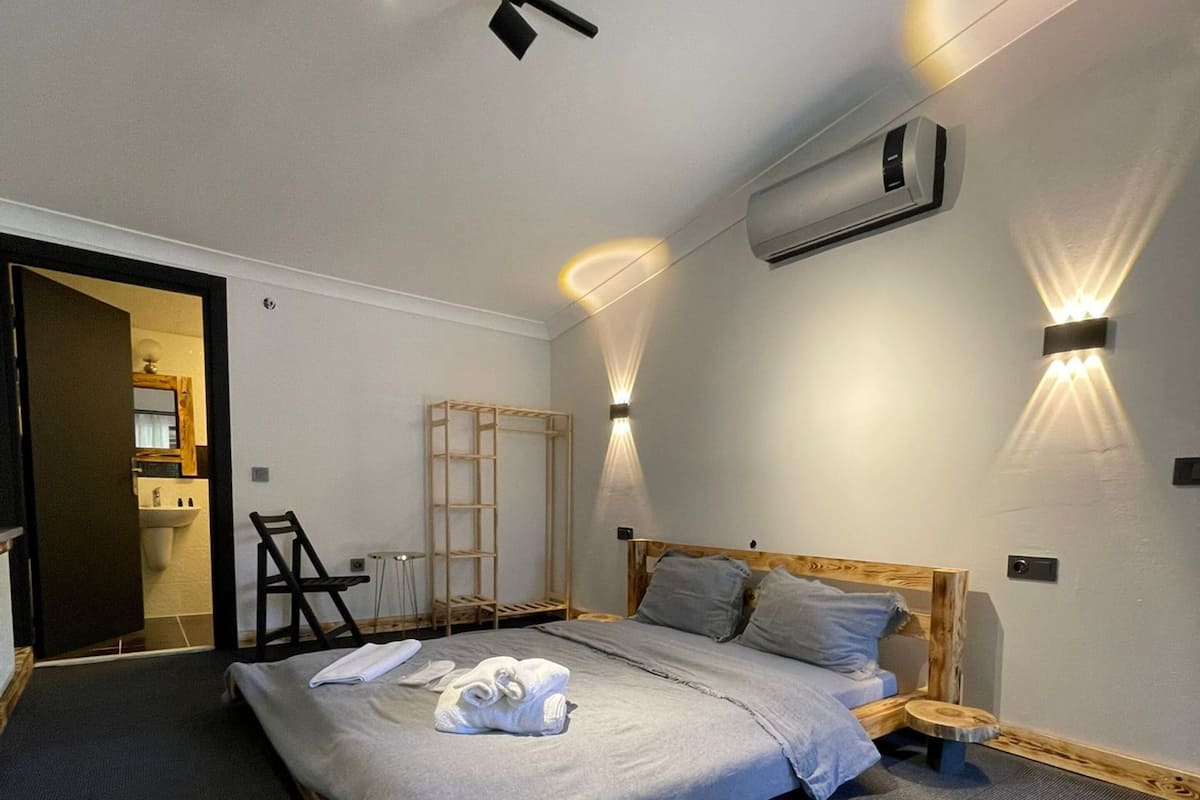 Ein modernes Schlafzimmer mit einem Bett, einer Holzleiter, einem kleinen Hocker und einer Wandklimaanlage.