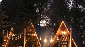 Un espace extérieur accueillant, aménagé avec des chaises en bois et un foyer, entouré d’une clôture en bois et d’arbres.