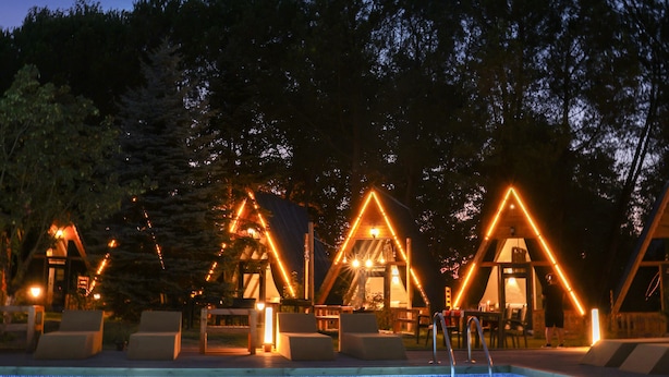 Une piscine avec une terrasse en bois et, en arrière-plan, des structures triangulaires illuminées.