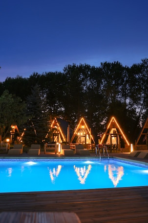 A swimming pool with wooden deck and triangular lighted structures in the background.
