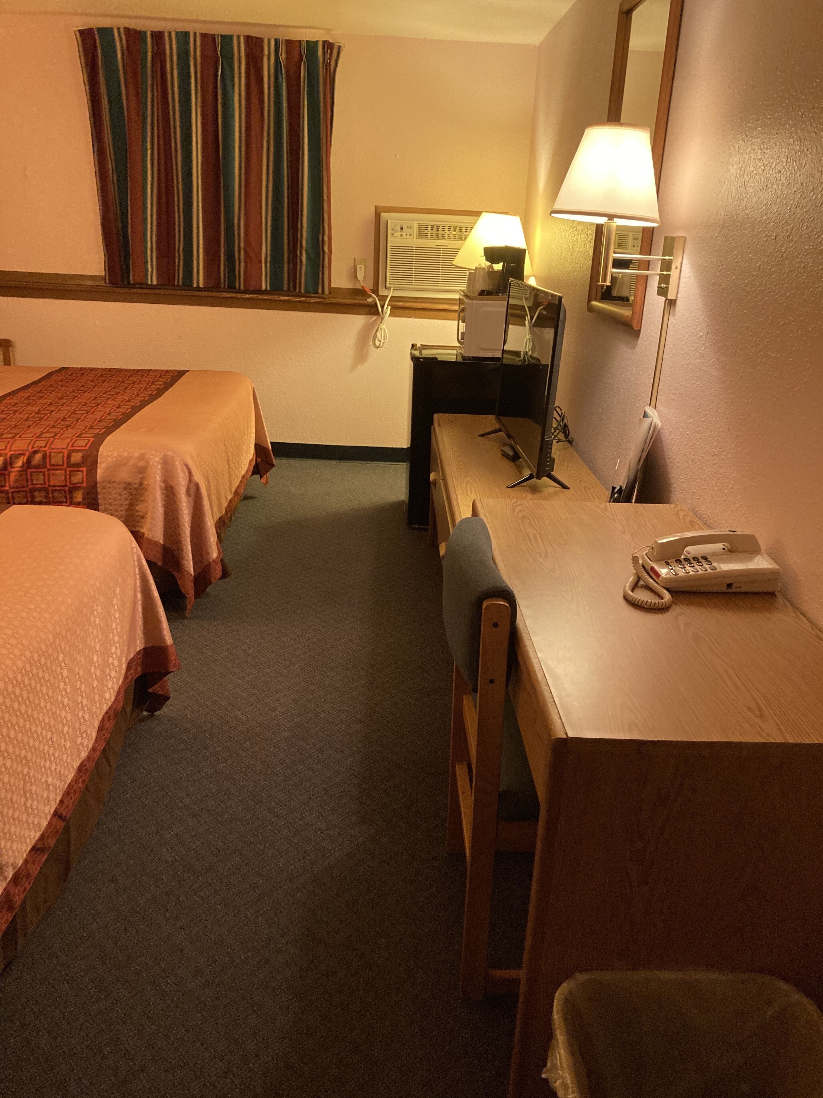 A hotel room with two beds, a desk with a telephone, a lamp, and a mirror.