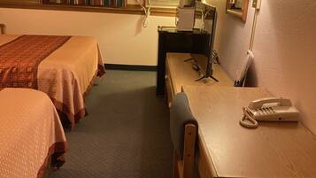 A hotel room with two beds, a desk with a telephone, a lamp, and a mirror.