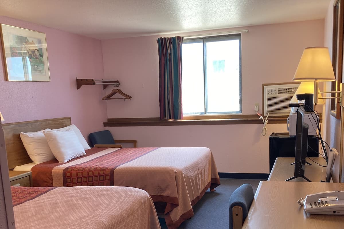 A hotel room with two beds, a desk, a telephone, a lamp, and a window with curtains.