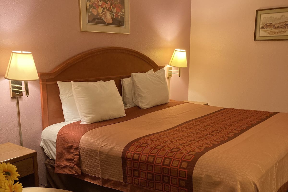 A hotel room with a bed, two bedside lamps, a wooden nightstand with a vase of flowers, and a round table.