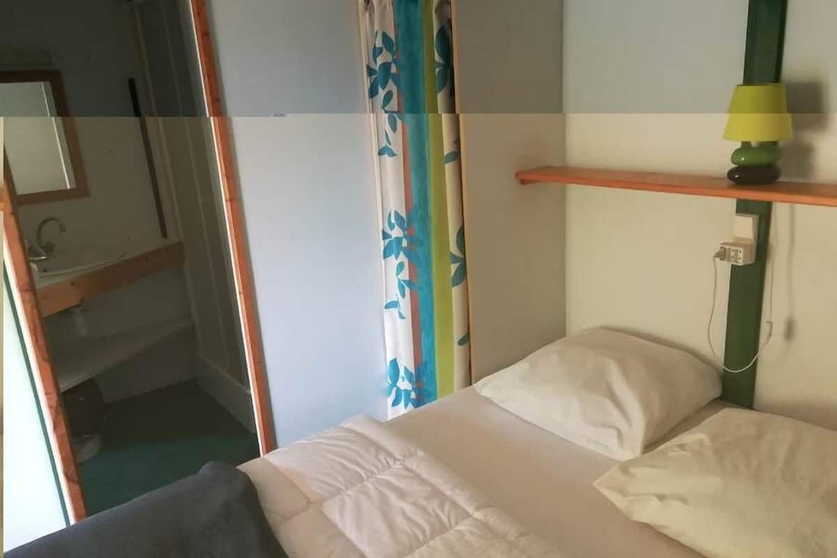 Une chambre à coucher avec un lit, une table de chevet avec une lampe, un miroir et une fenêtre avec des rideaux.