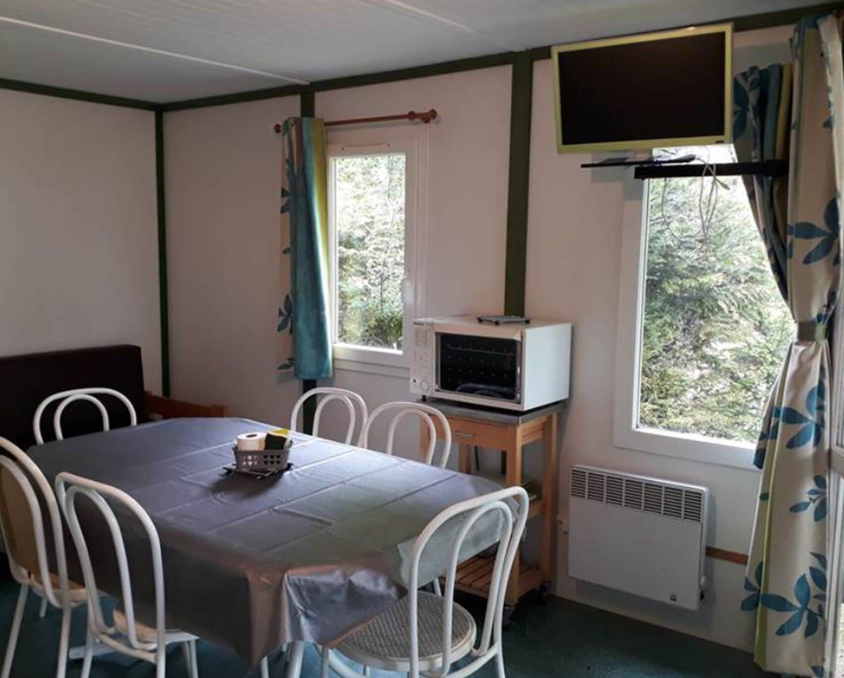 A room with a table, chairs, a television, and a window with curtains.