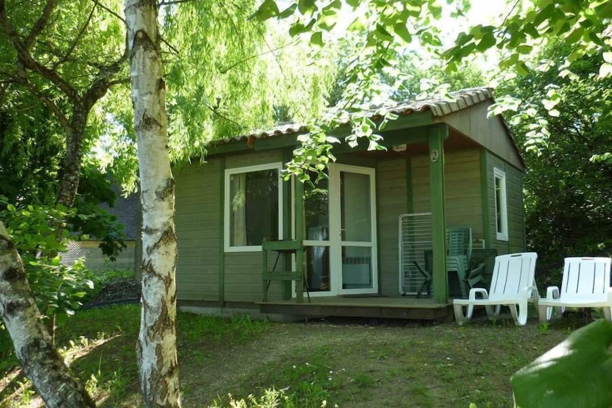 Une petite cabane à un seul étage, dotée d’un porche et de deux chaises blanches.